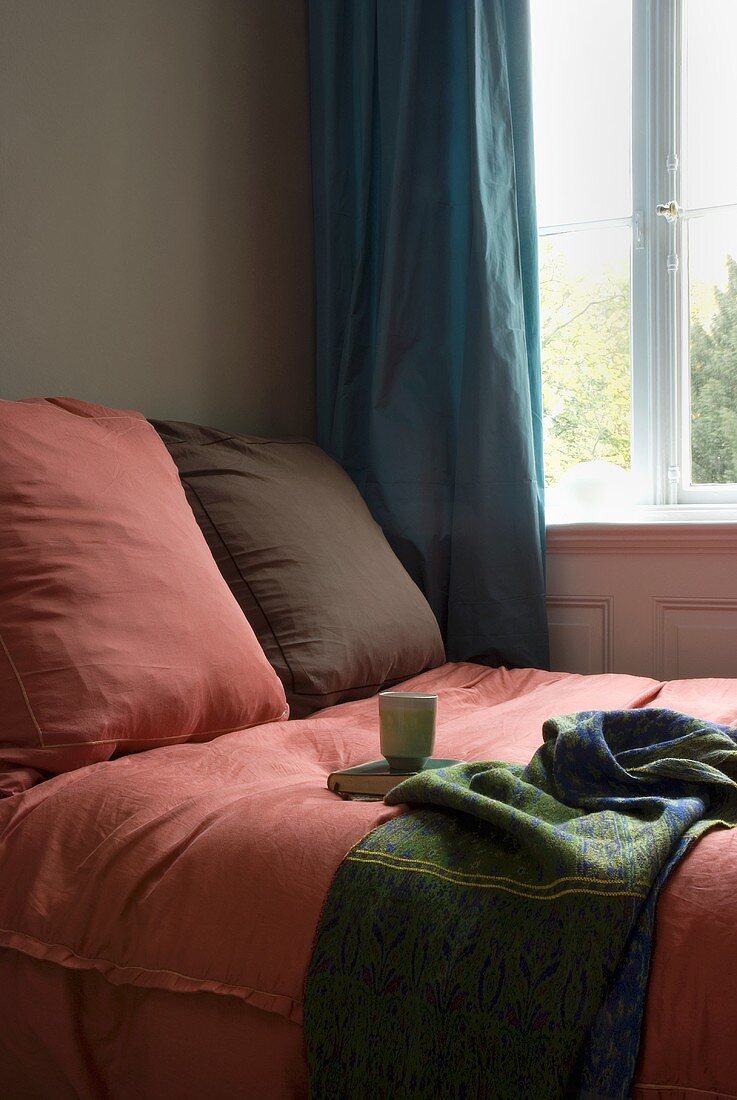 Pink and brown cushions on a bed in front of a window