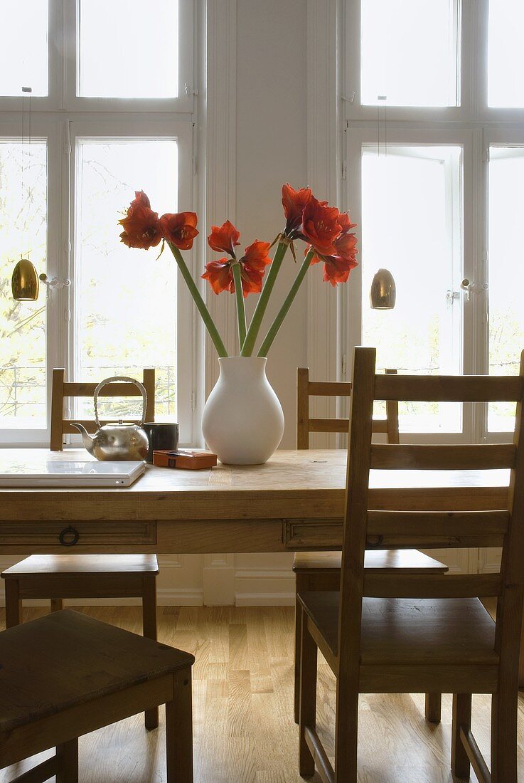Esstisch aus Holz mit roter Amaryllis in weisser Vase vor Fenster