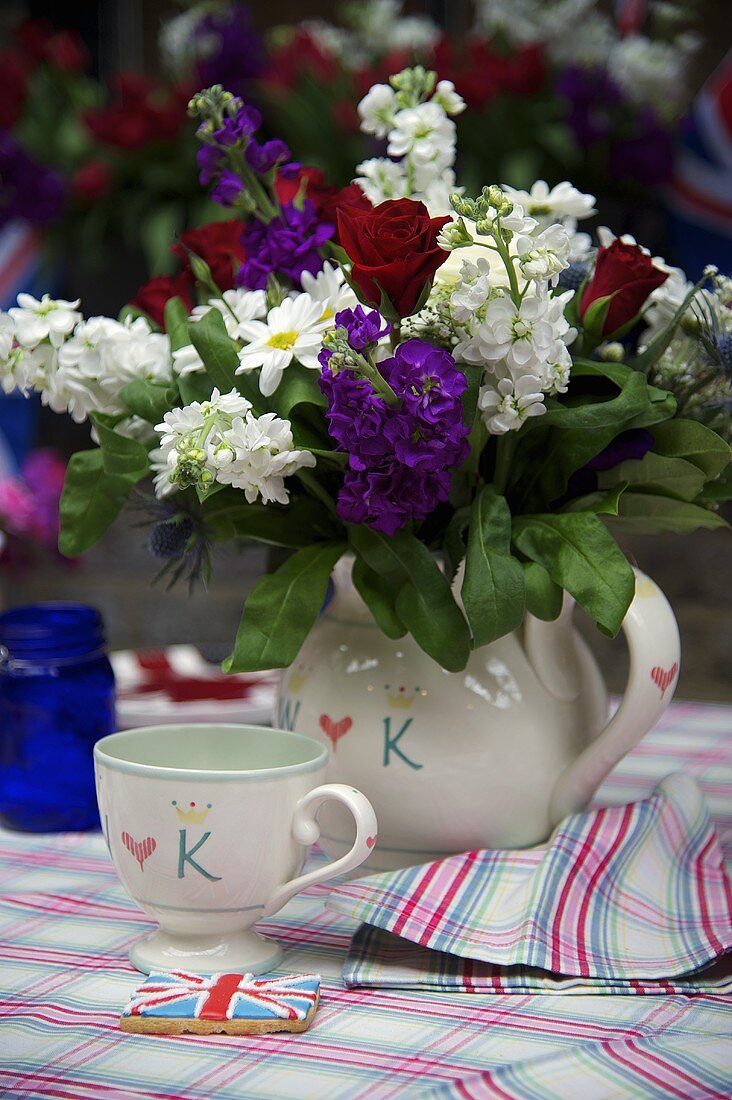A bunch of flowers in a white ceramic jug and a matching cup