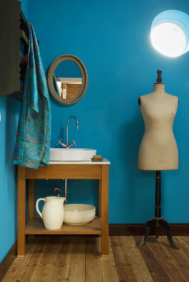 Corner of a room painted blue with a wash stand and dressmakers mannequin under a circular skylight
