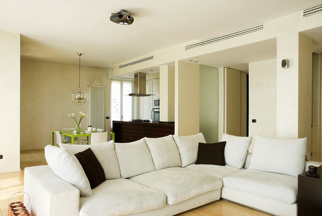 Weisses Sofa übereck mit braunen Kissen im offenen Wohn- und Essbereich