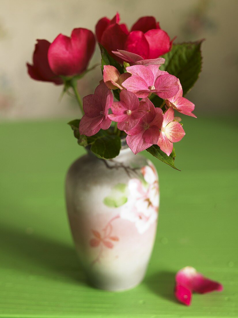 Flowers with pink blossoms in a porcelain vase on a green surface