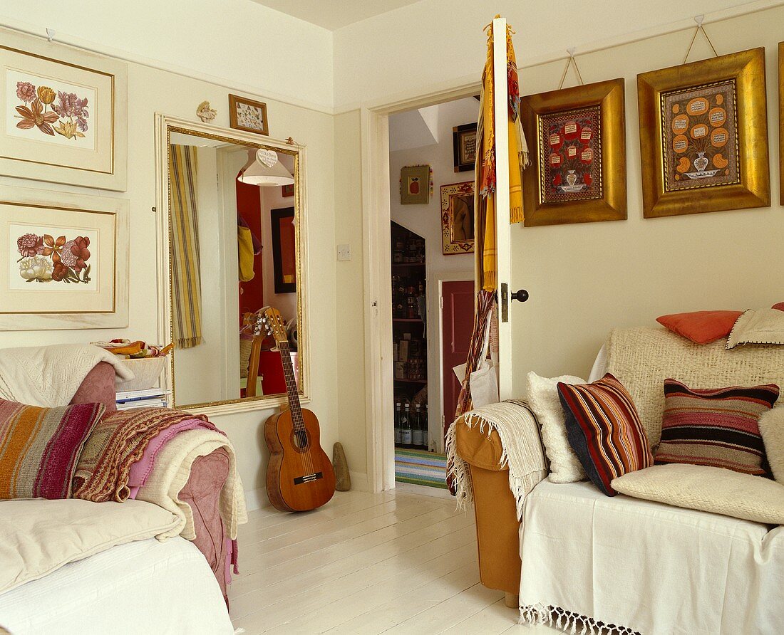 Ländliches Wohnzimmer mit Polstermöbeln und gerahmten Blumenmotiven neben offener Zimmertür