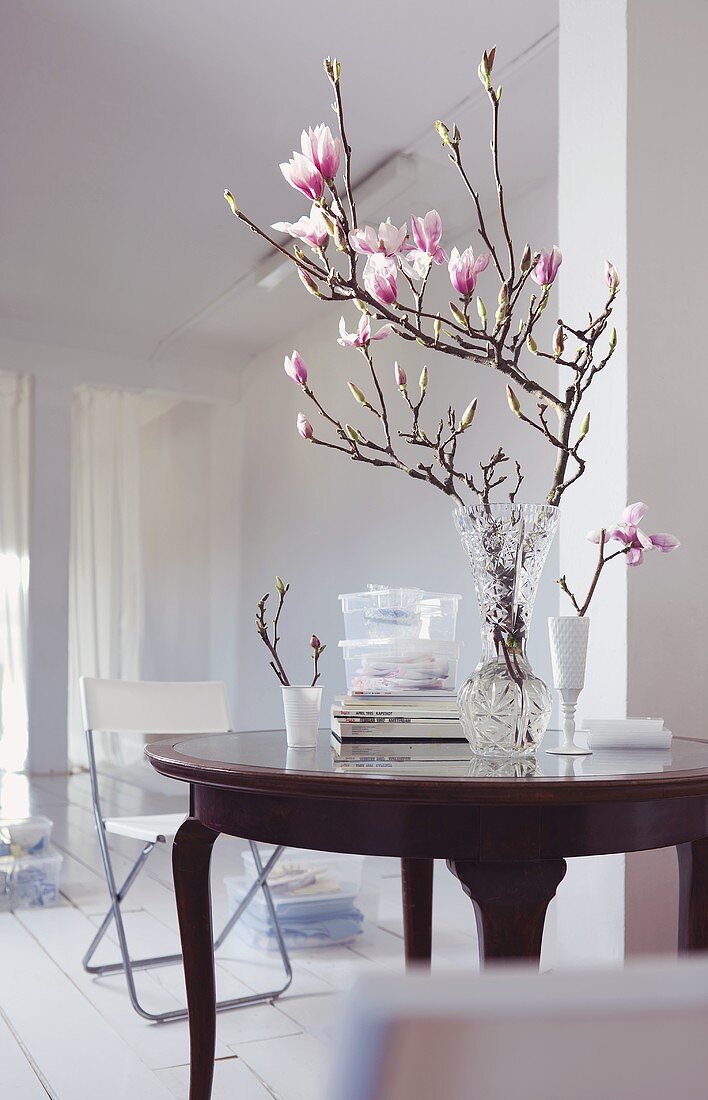 Magnolienzweig in Glasvase auf antikem Tisch im weissen Raum