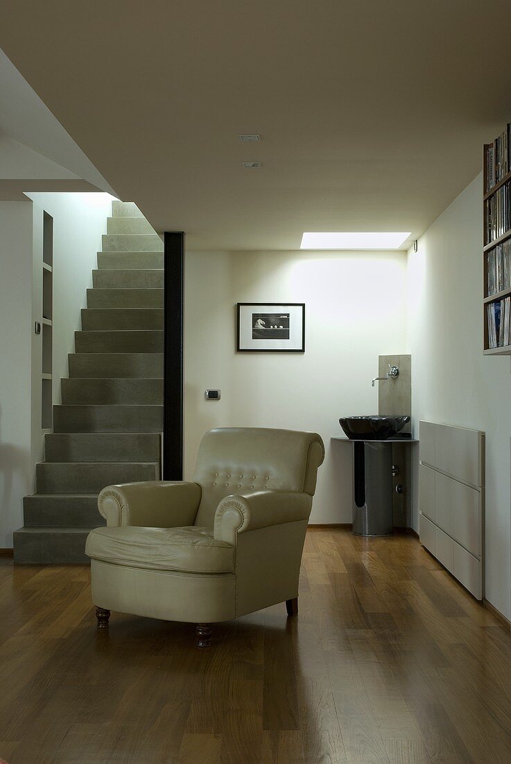 A light leather armchair in an open living room with a staircase