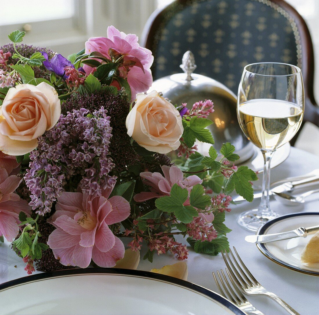 Frühlingsstrauss mit rosa Rosen und lila Flieder auf einem festlich gedeckten Tisch