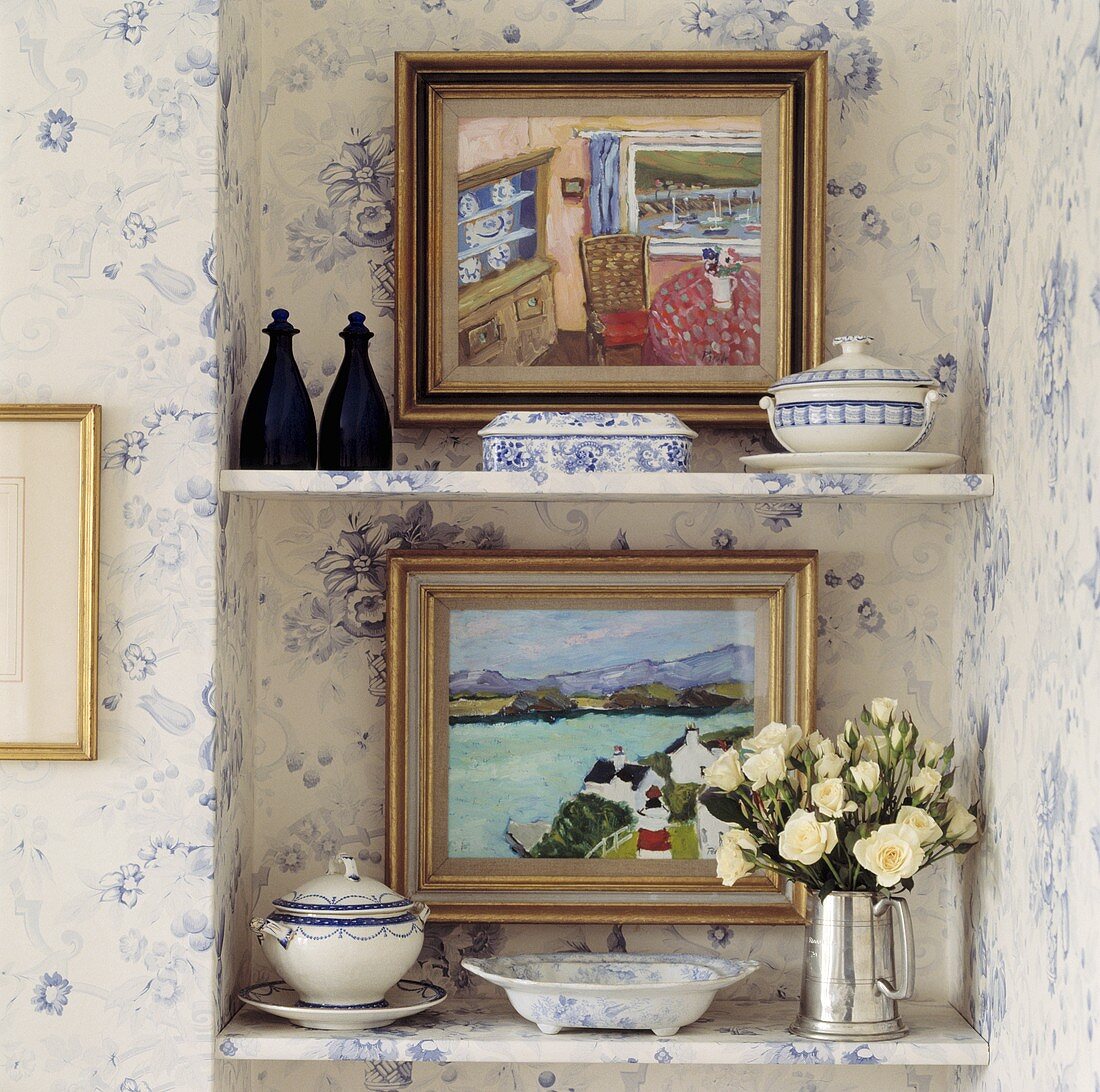 Bilder, blau-weisses Porzellan und Silberkanne mit weißen Rosen auf Regalen in einer Wandnische