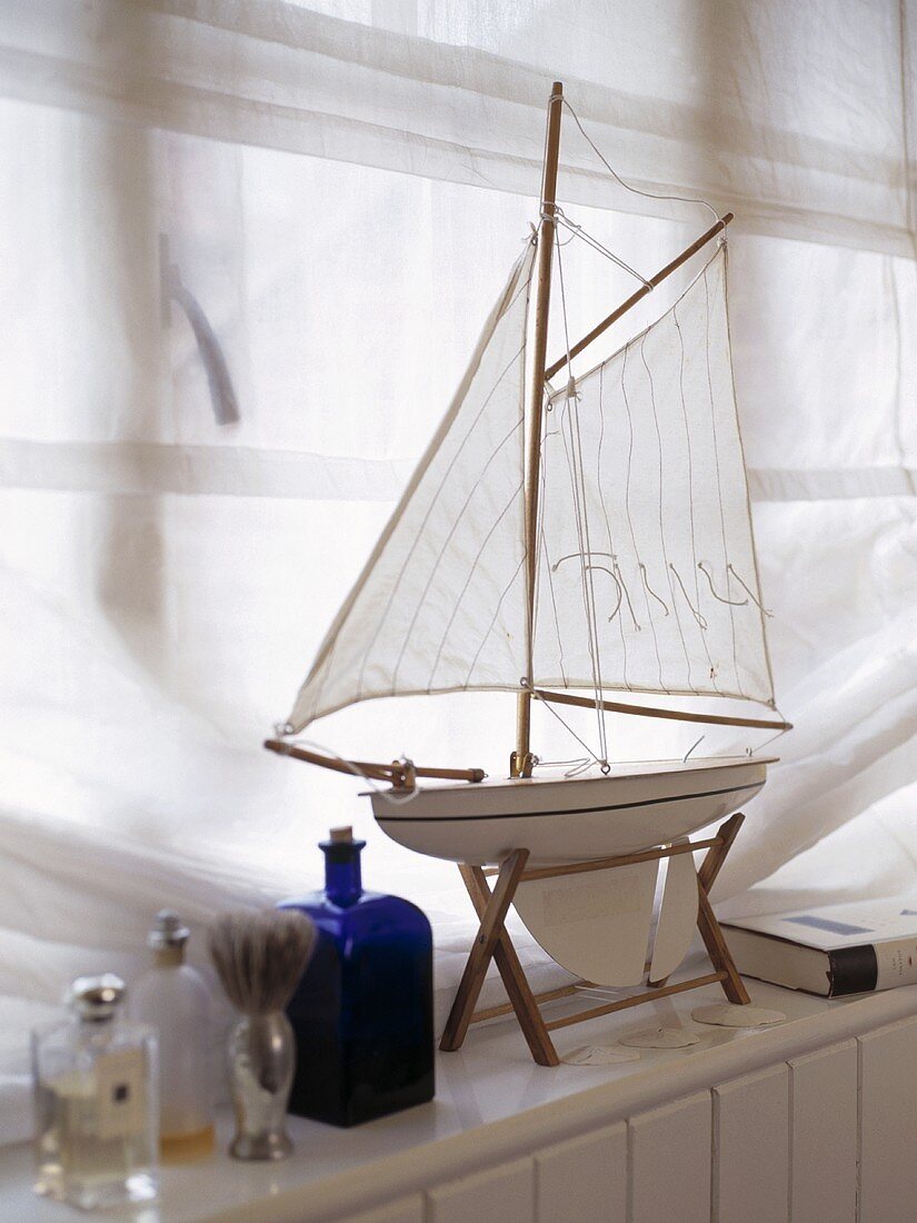 Modellboot auf Fensterbank und weißer Vorhang
