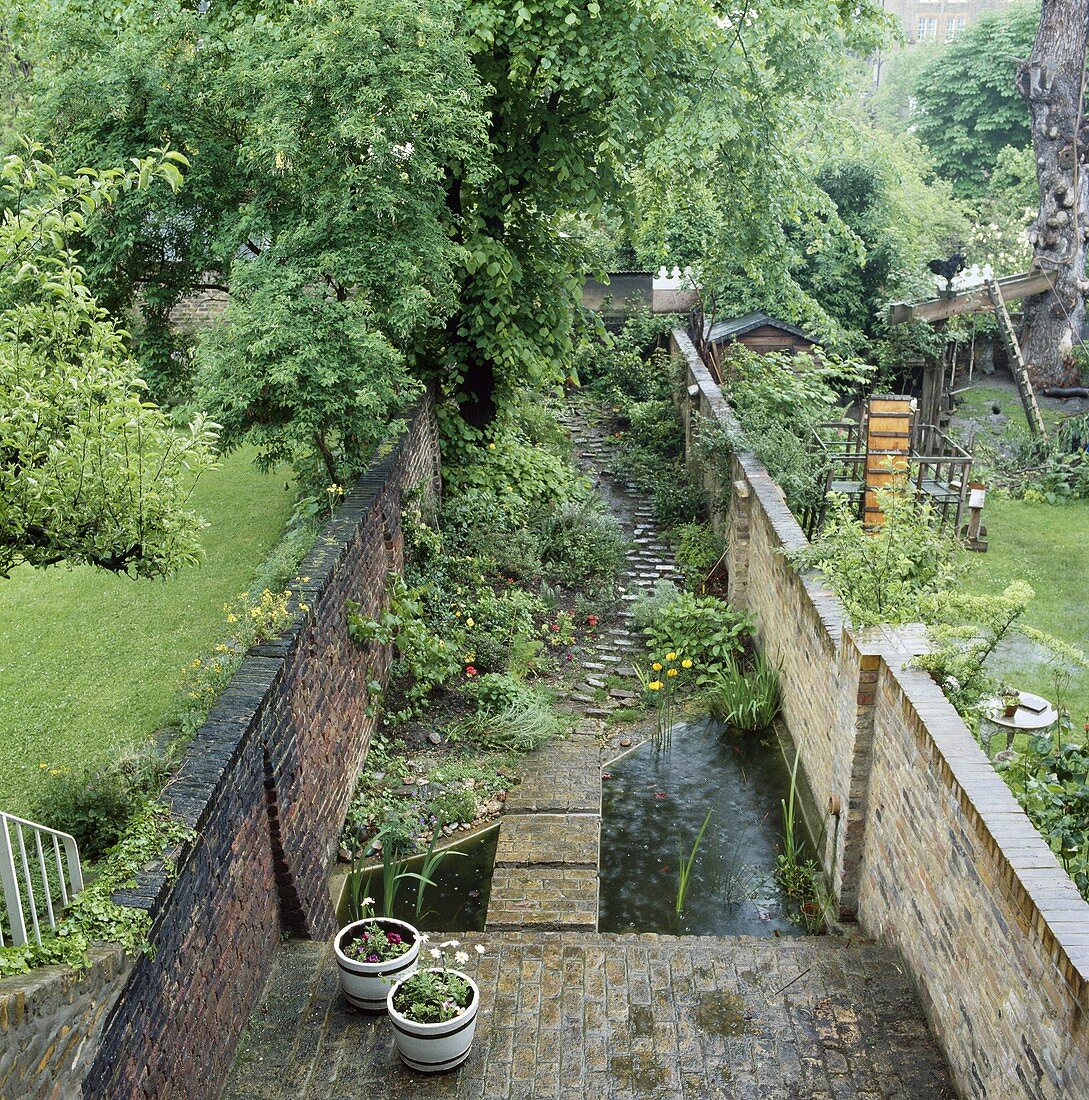 Schmaler Stadtgarten mit Steinmauern und Steg über Teich