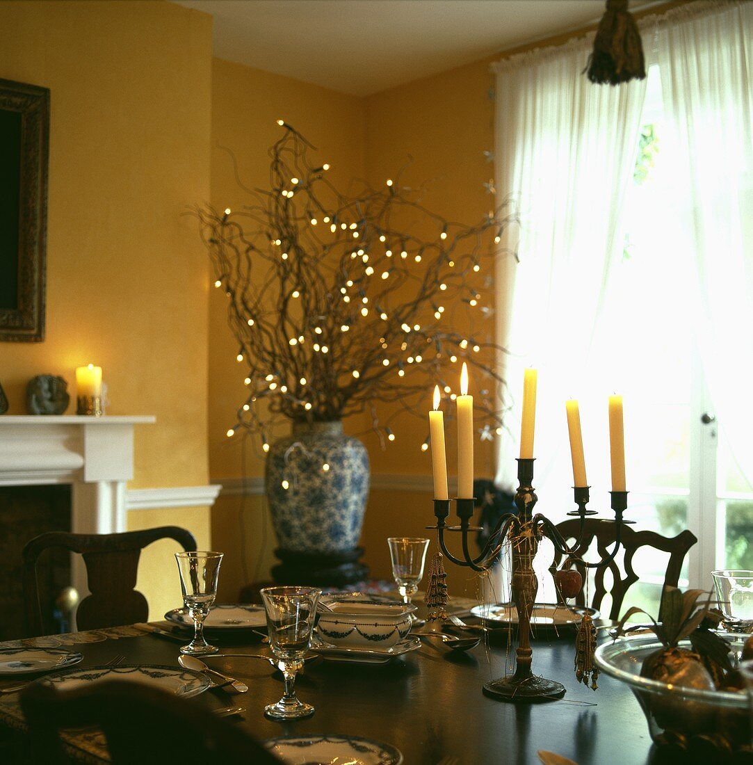 Kerzenleuchter auf gedecktem Tisch und Lichtdeko in Vase im gelben Esszimmer