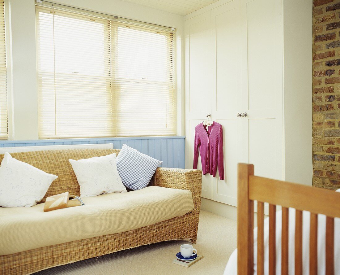 Sofa aus Rattan vor Fenster mit geschlossener Jalousie und Einbauschrank in Schlafzimmerecke