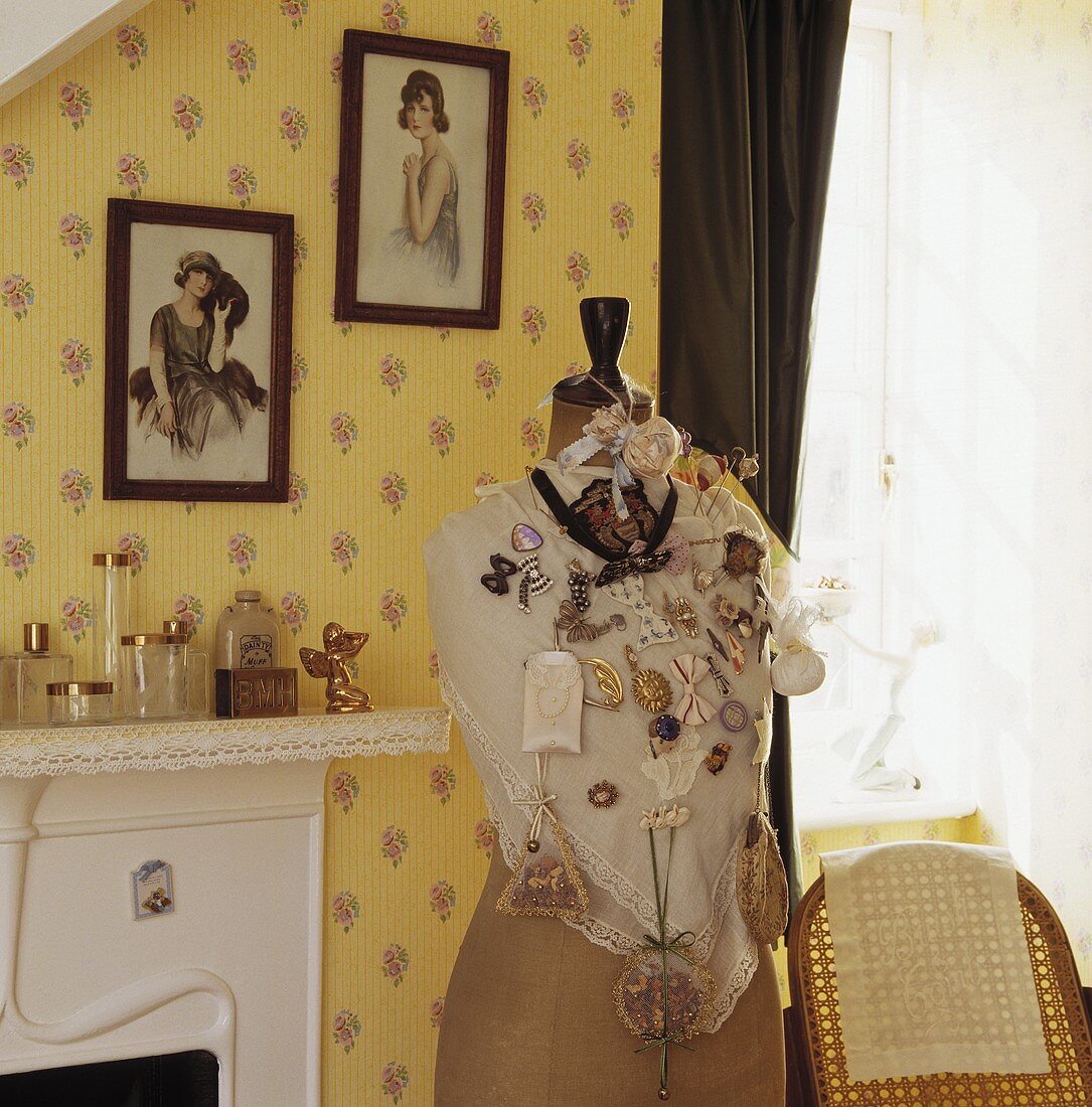 Schlafzimmer mit gelber Tapete und Blumenmuster, einer mit Broschen behängten Schneiderpuppe und Bilder aus den dreißiger Jahren an der Wand über dem Kamin