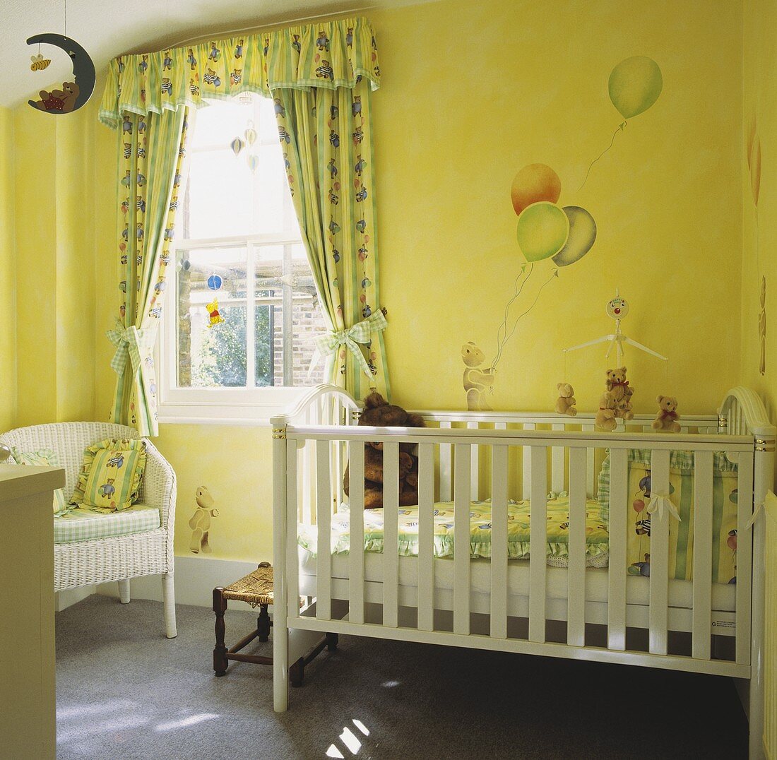 Kinderzimmer mit weißem Kinderbett, mit aufgemalten Luftballons an der Wand und Fenstervorhängen in grün-gelbem Muster