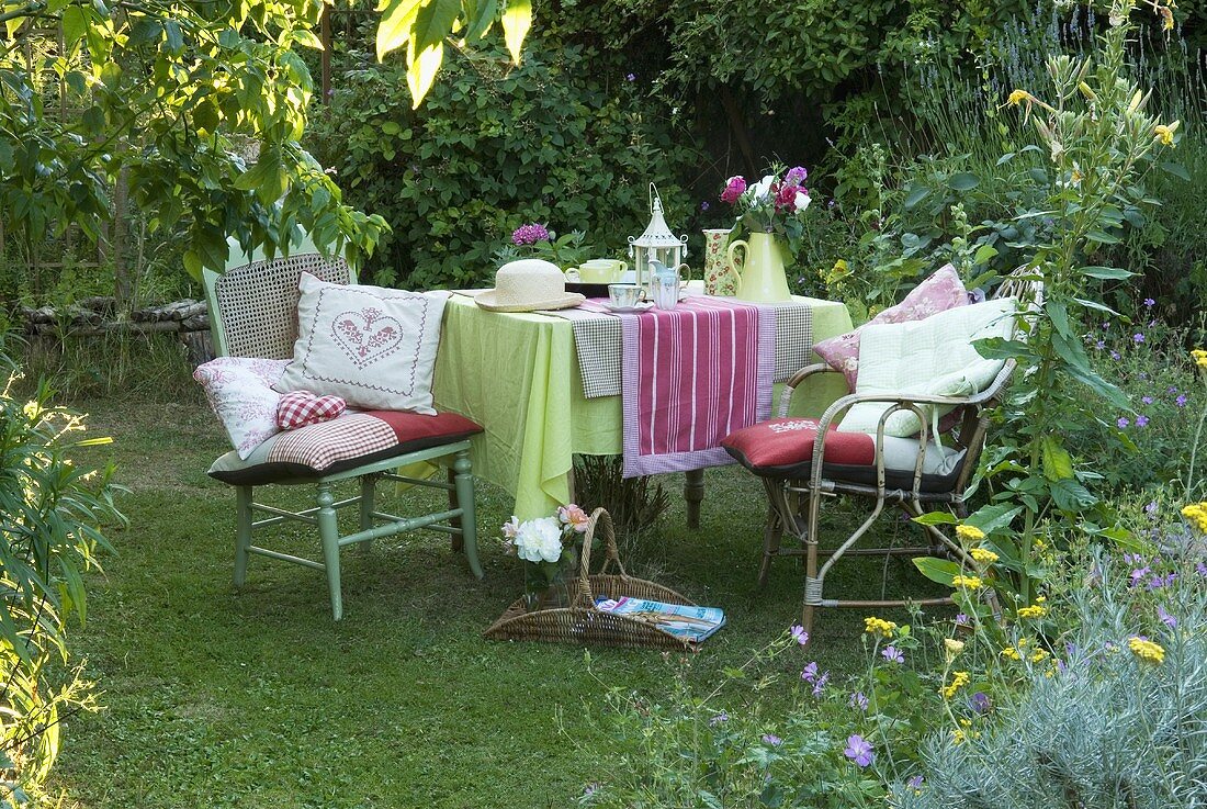 Tisch mit Decken und Stühlen mit Kissen auf dem Rasen im Garten am frühen Abend