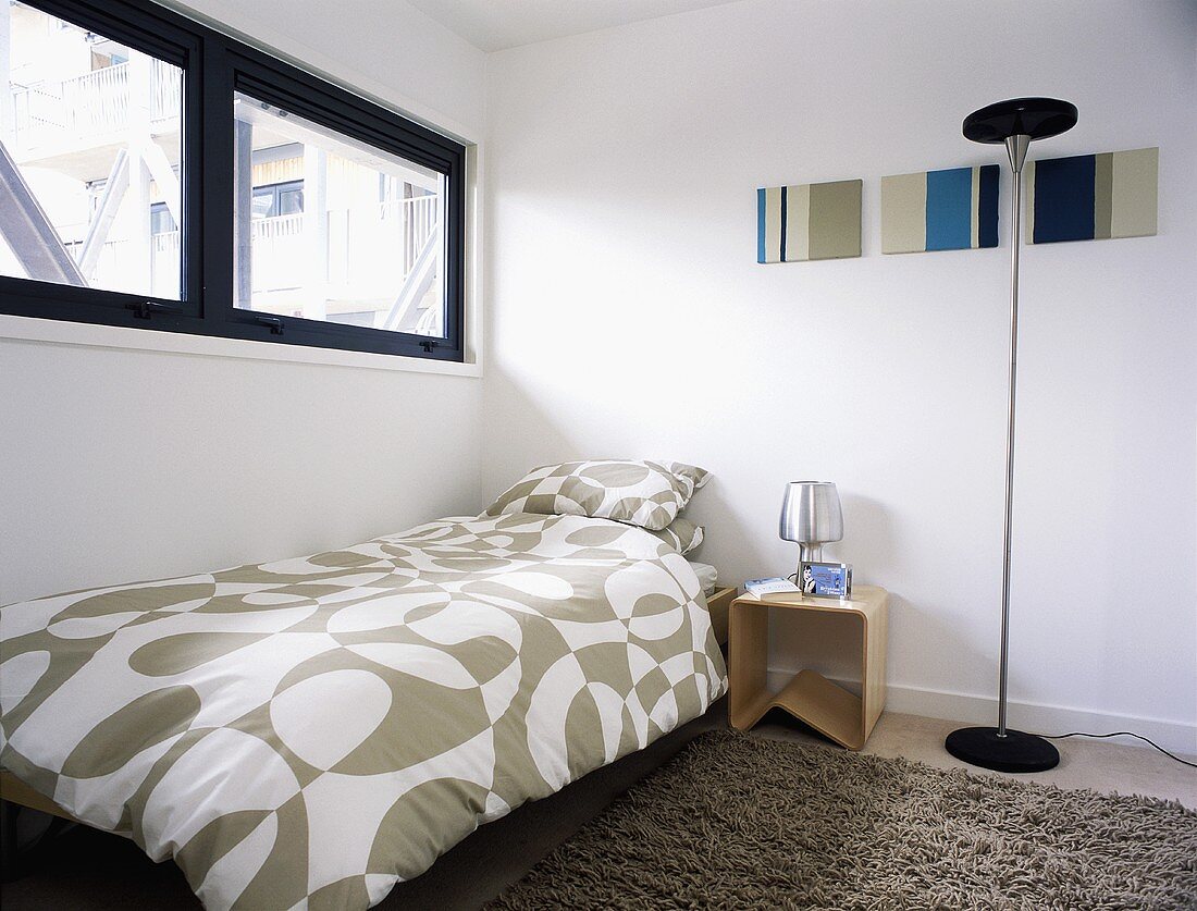 A modern bedroom with a transom window and a single bed with patterned bedclothes