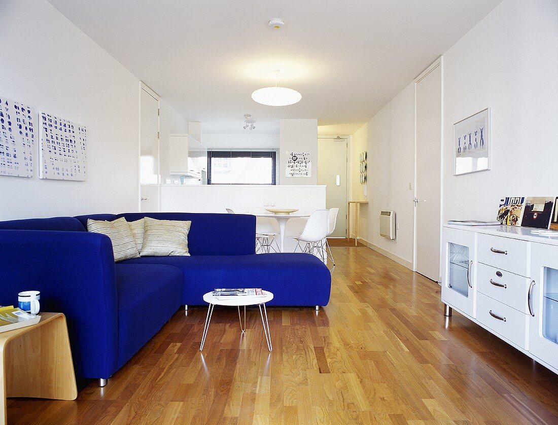 A white, open-plan living room with a blue corner sofa