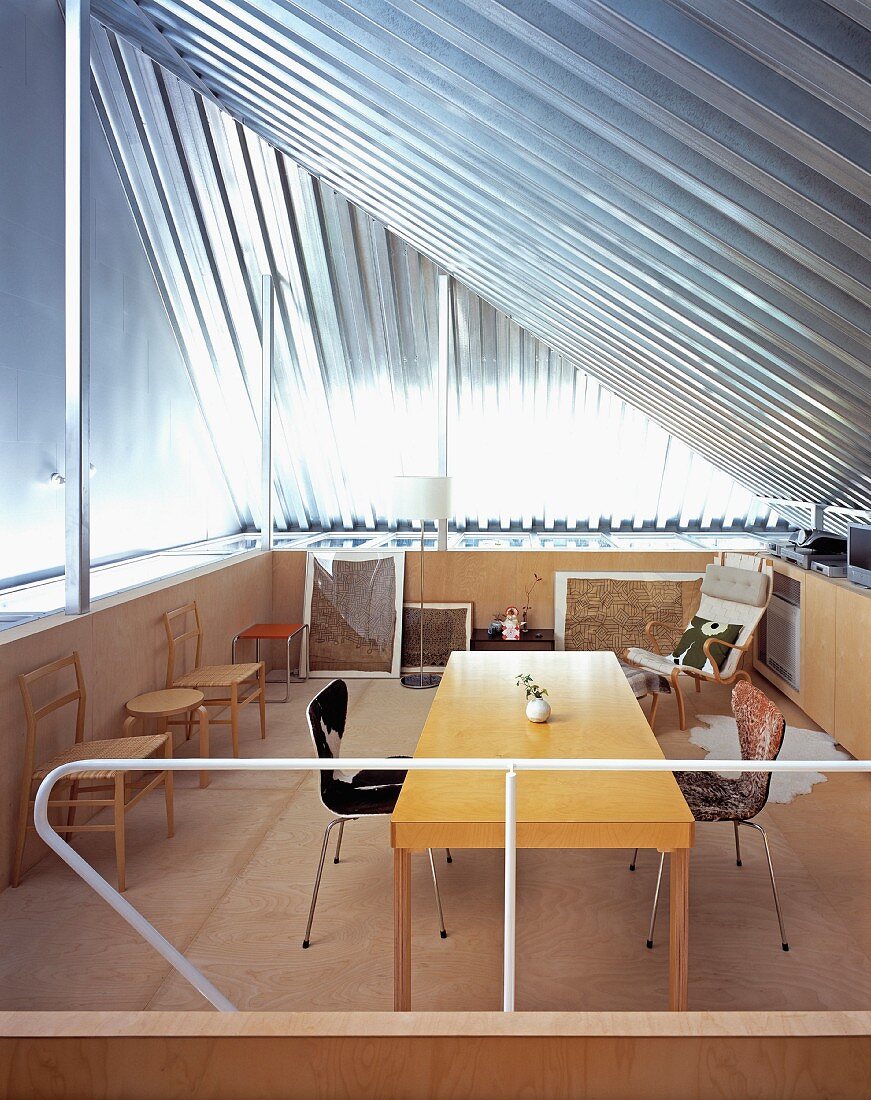 Offener Raum unter Dach mit Metallverkleidung und Holztisch mit verschiedenen Stühlen