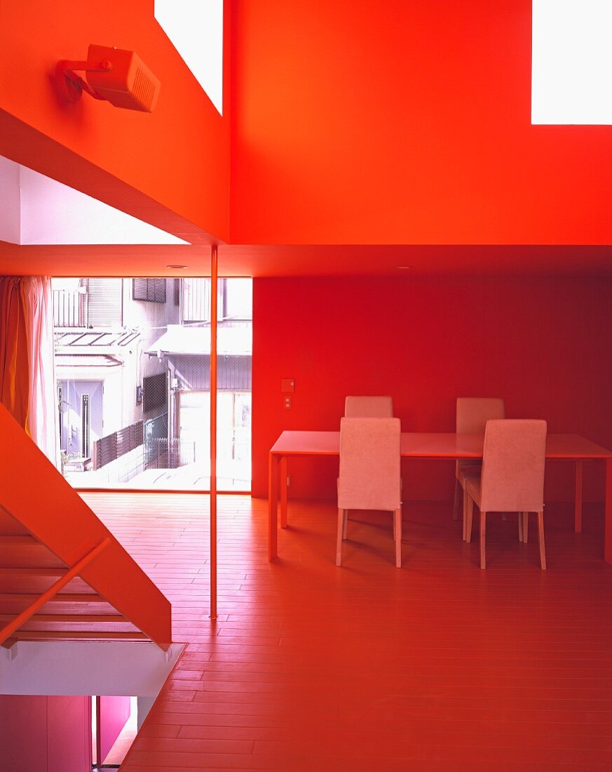 A dining table and chairs next to a floor-to-ceiling window in an open-plan, red-painted living room