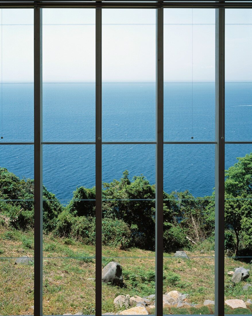 Blick durch das Fenster in den Garten und auf das Meer