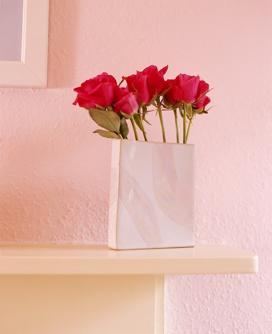 Rote Rosen in rechteckiger Vase vor rosa Wand