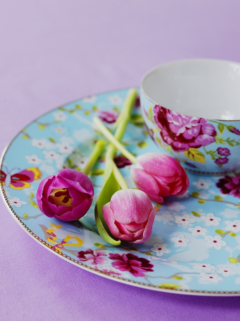 Tulpen neben Schale auf Teller mit Blumenmuster