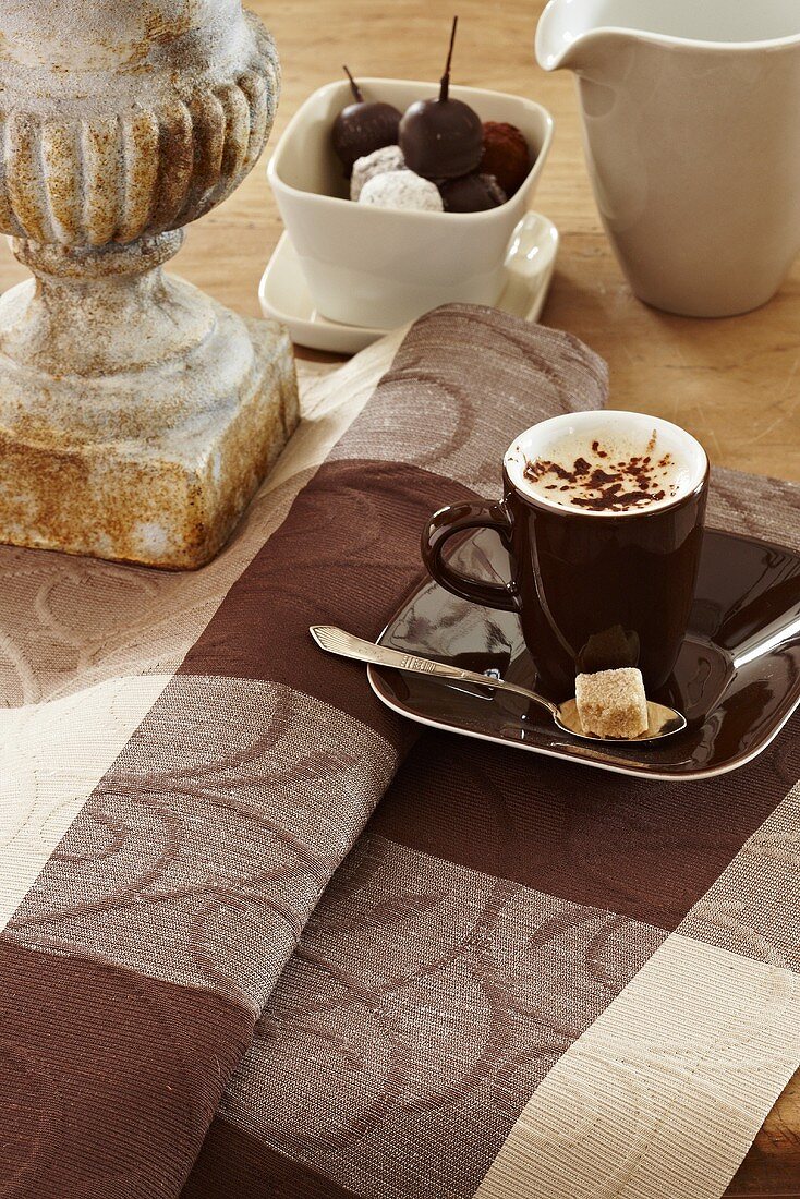 A cup of cappuccino on a brown checked table cloth