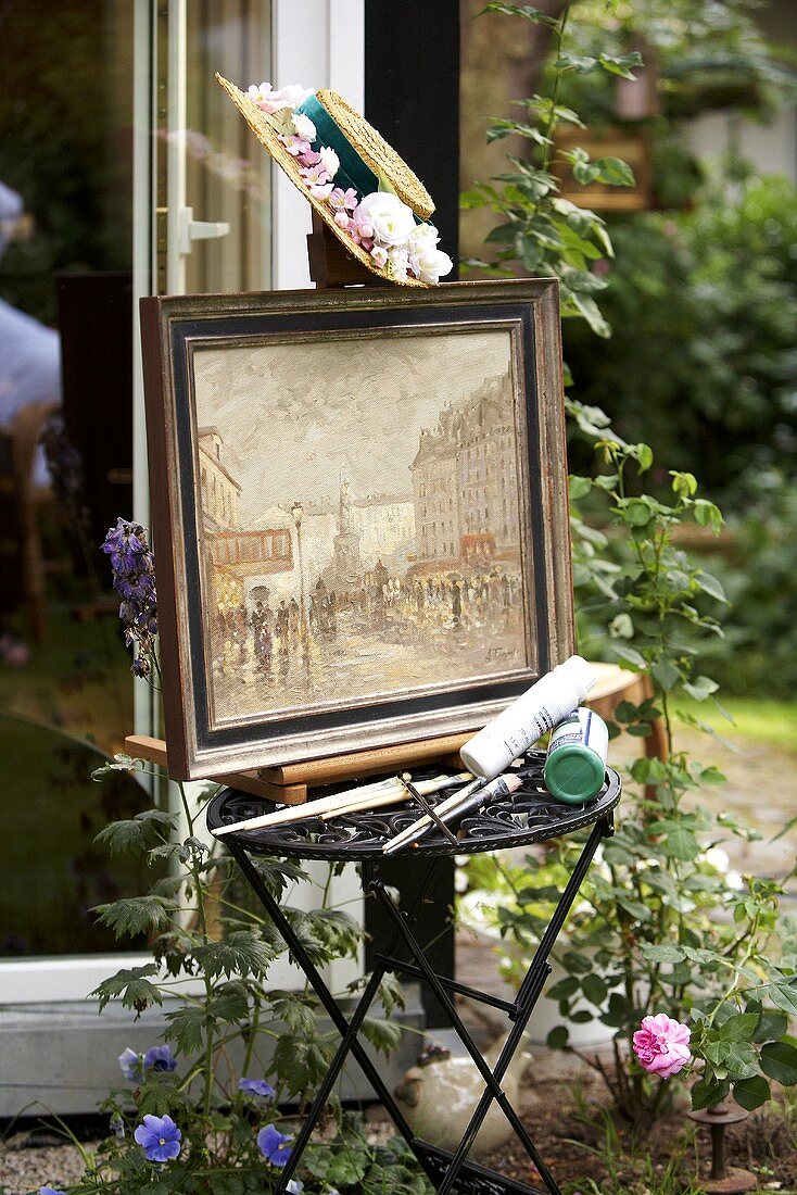 A framed picture and painting utensils on a small table in the open air
