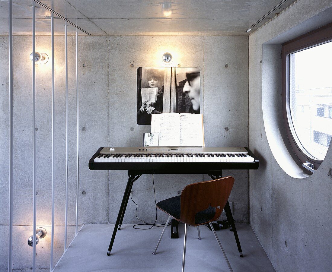 A music room with a keyboard and a chair against an exposed concrete wall