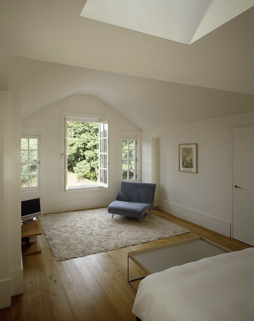 Minimalistischer weisser Schlafraum mit Sessel neben offener Terrassentür