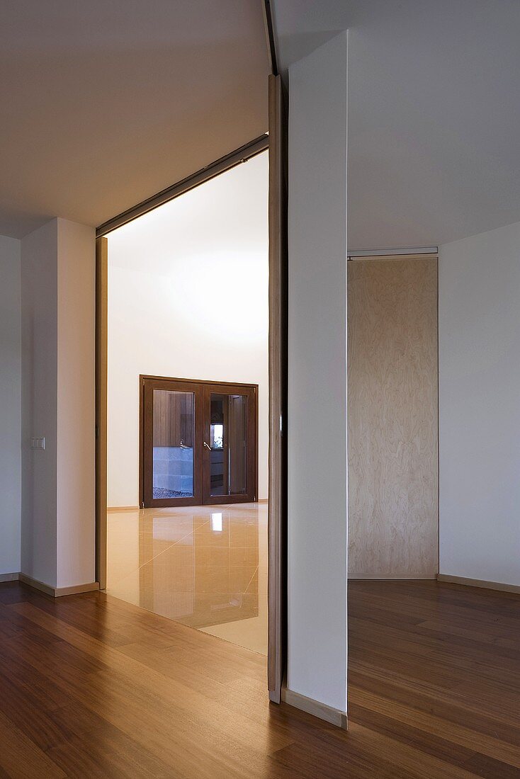 A modern anteroom with parquet flooring and an open doorway with a view into an empty room
