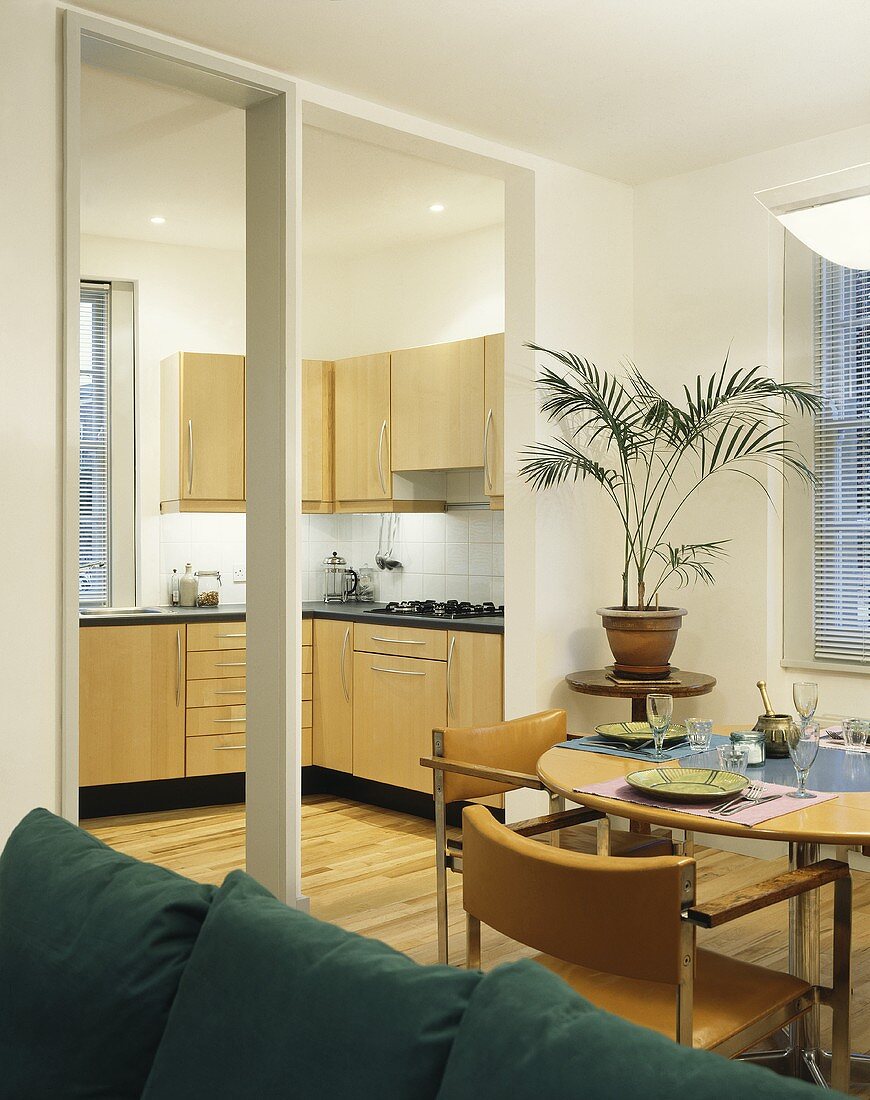 A dining room with an open doorway and a view of a kitchen with wooden cupboards