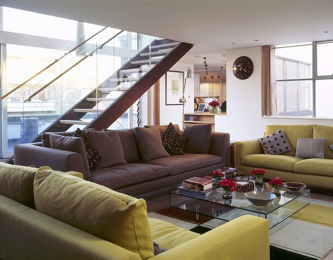 Different coloured sofas in front of a glass table with an open staircase in an open-plan living room