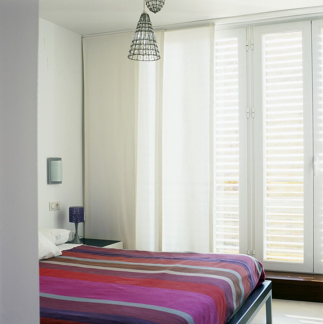 Modernes Schlafzimmer mit gestreifter Tagesdecke auf Doppelbett und mit Flächenvorhang