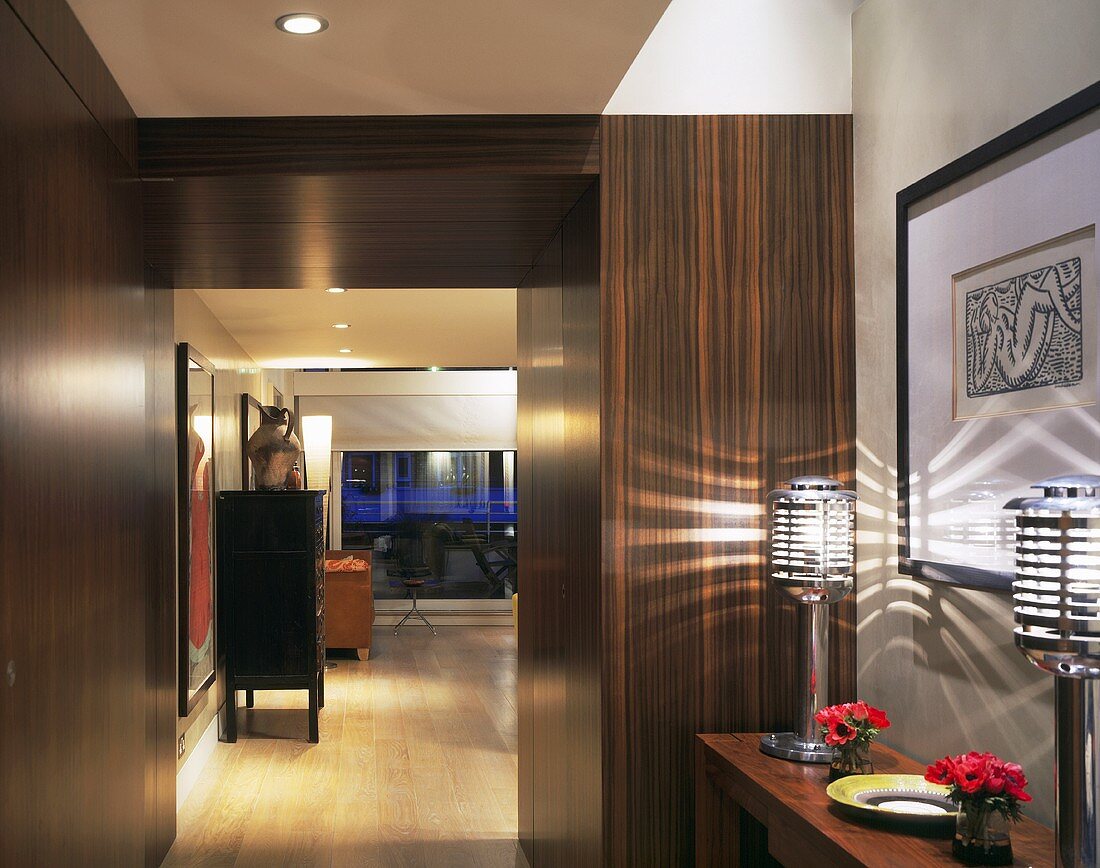 A hallway with built-in cupboards made of tropical wood and a view through an open doorway into a living room