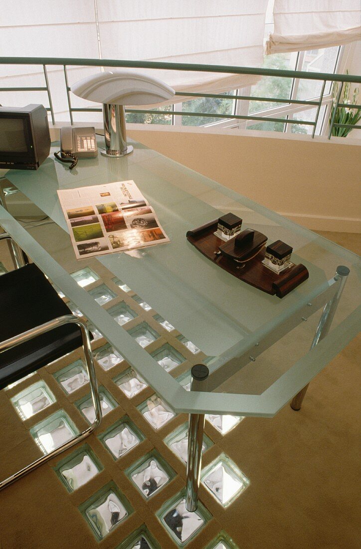 Moderner Arbeitsplatz mit Glastisch und Freischwinger-Stuhl auf Galerie mit Glasbausteinen im Boden