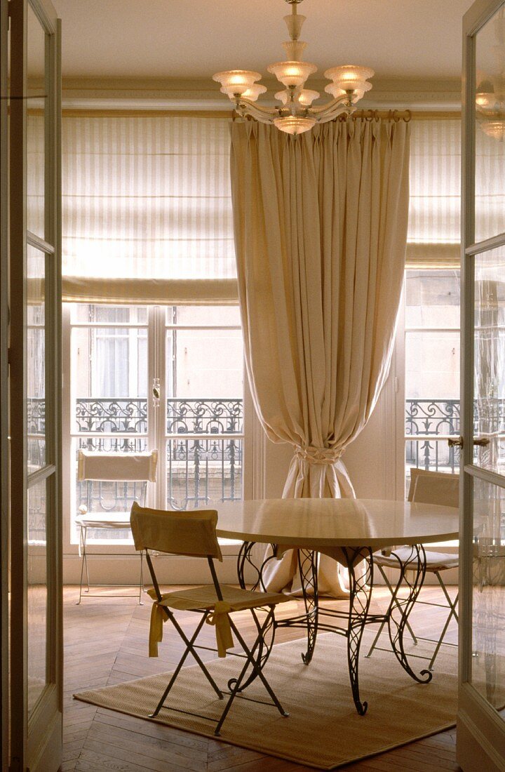 Gartenstühle an rundem Tisch mit geschwungenen Metallfüssen vor Rollos und Vorhang in leichtem, französischem Esszimmer