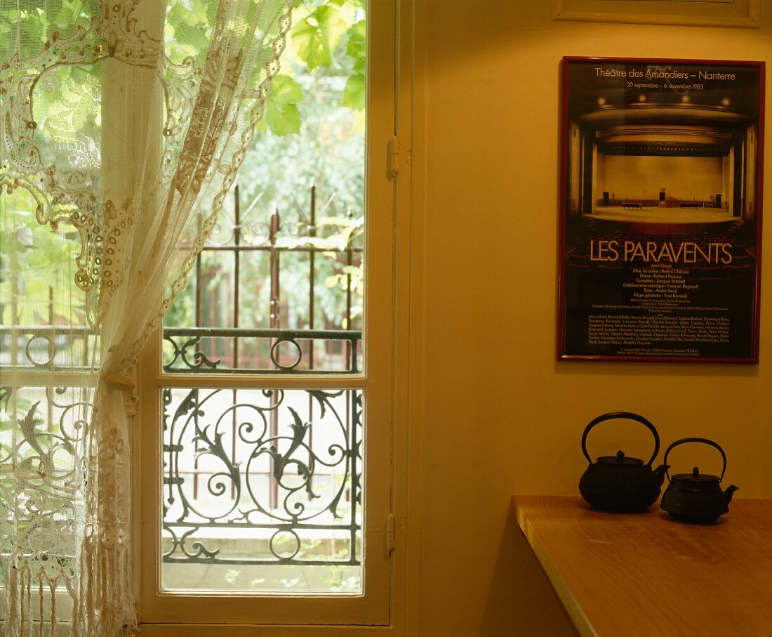 Japanische Teekannen unter Plakat an der Wand neben französischem Fenster mit Spitzenvorhang