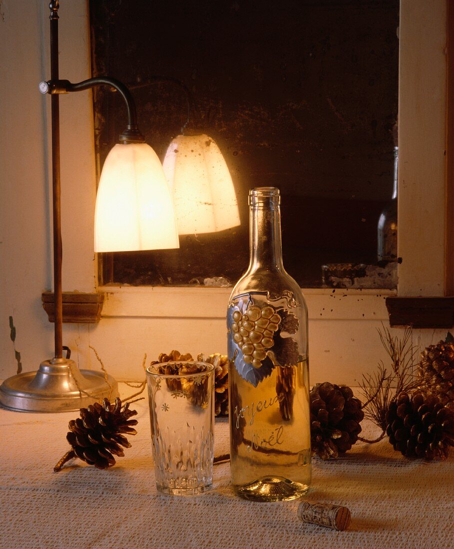 Brennende, antike Metalllampe, Weinflasche und Tannenzapfen vor blindem Spiegel
