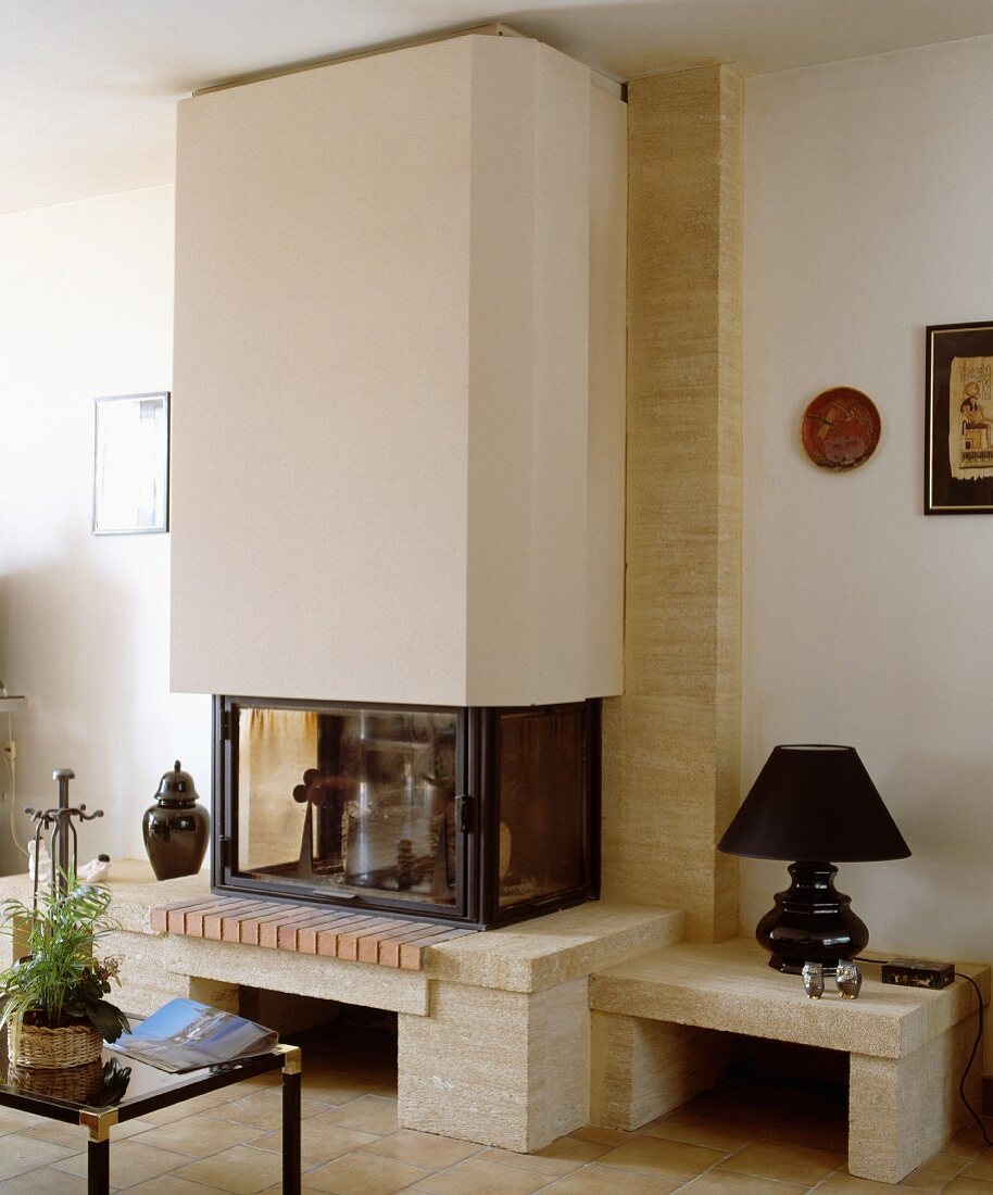 Kubischer Kamin mit schwarzer Lampe auf umlaufender Steinbank in modernem Wohnzimmer