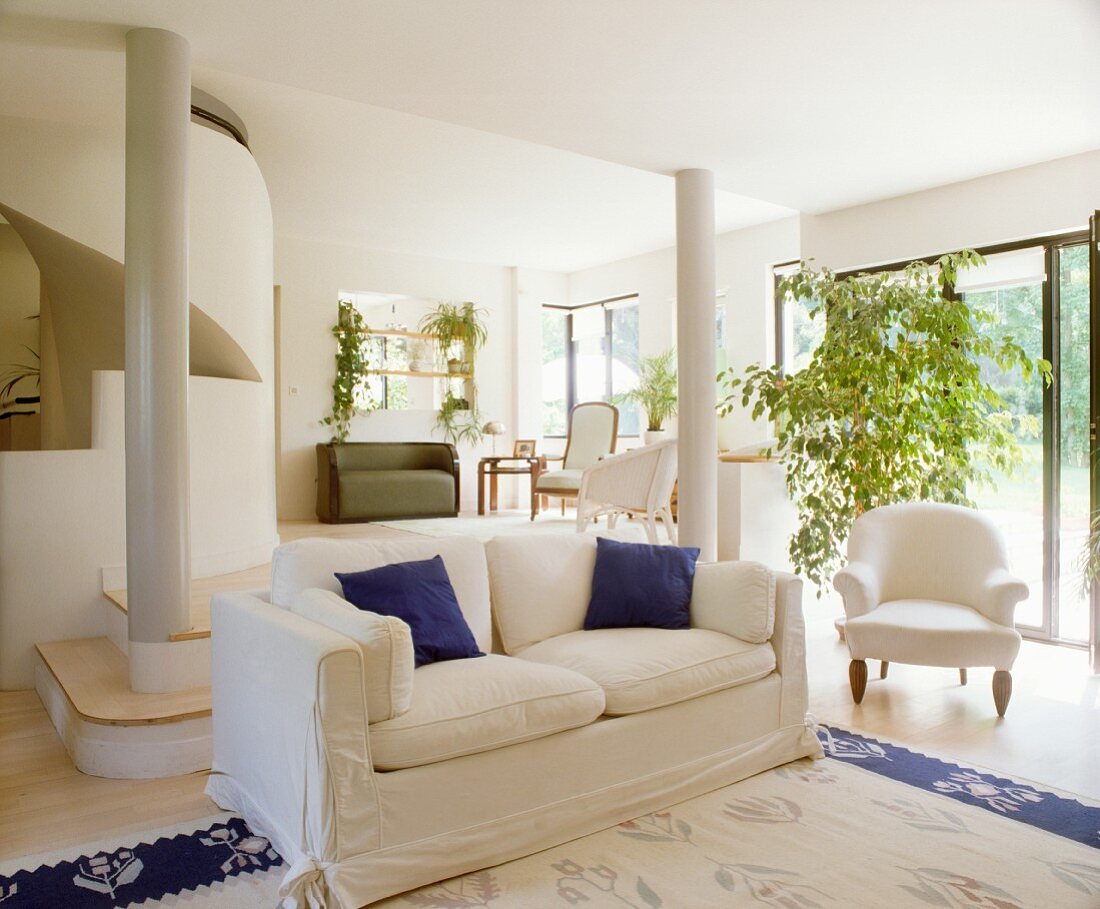 Blaue Zierkissen auf Sofa und blaue Teppichbordüre als Farbtupfer im Weiß des modernen, offenen Wohnzimmers