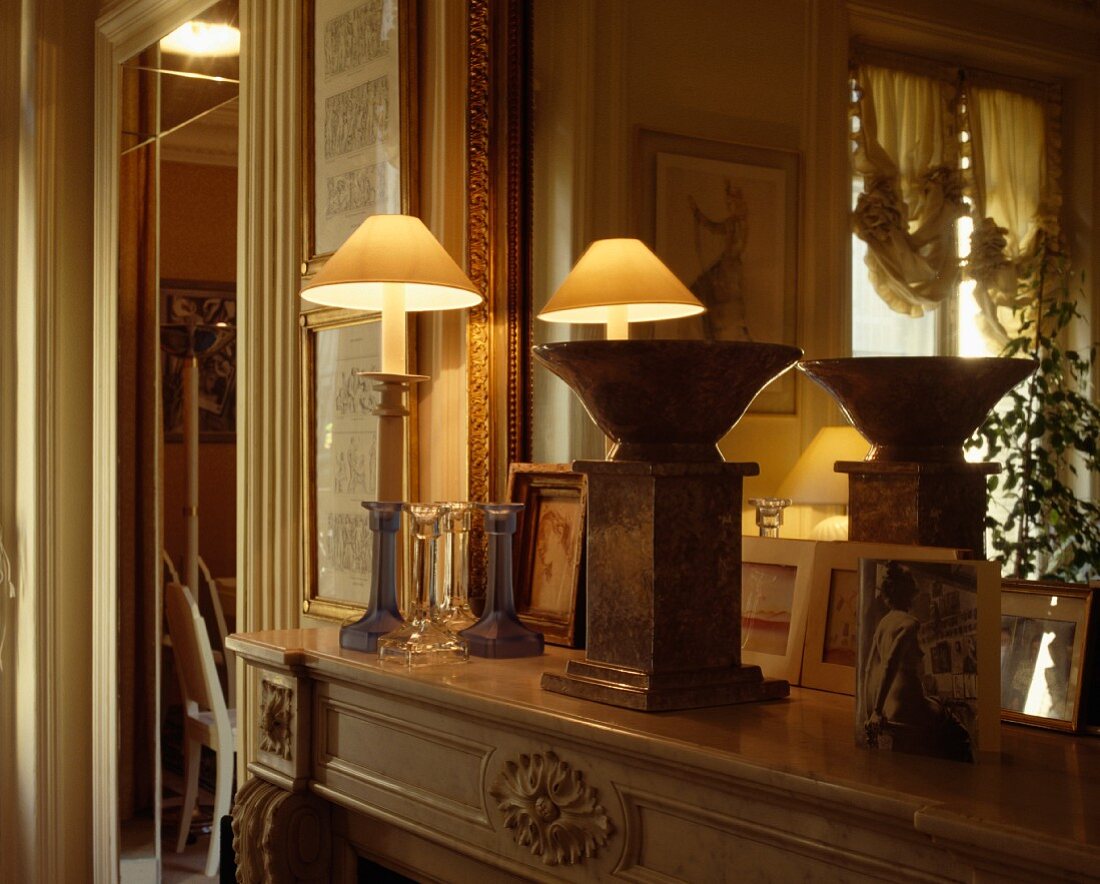 Brennende Lampe und Marmorschale mit Sockel auf antikem Kaminsims vor Spiegel
