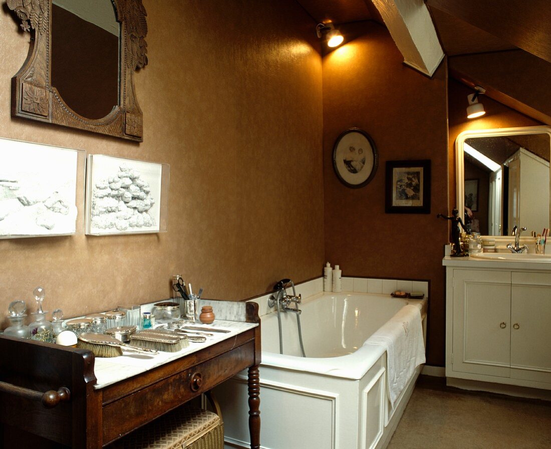 Wohnliches Badezimmer mit antiker Kommode und Spiegel neben weisser Wanne mit Kassettenverkleidung vor nougatfarbener Wand
