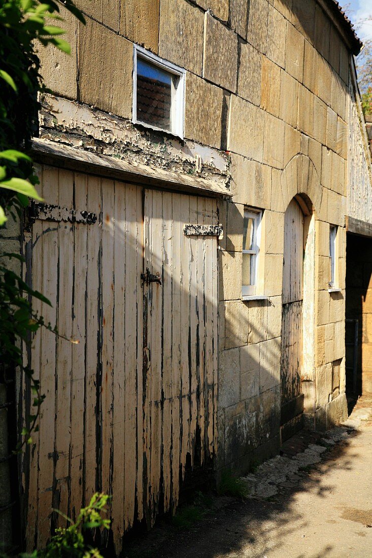 Baufälliges, altes Holztor in Natursteinfassade eines alten Landhauses