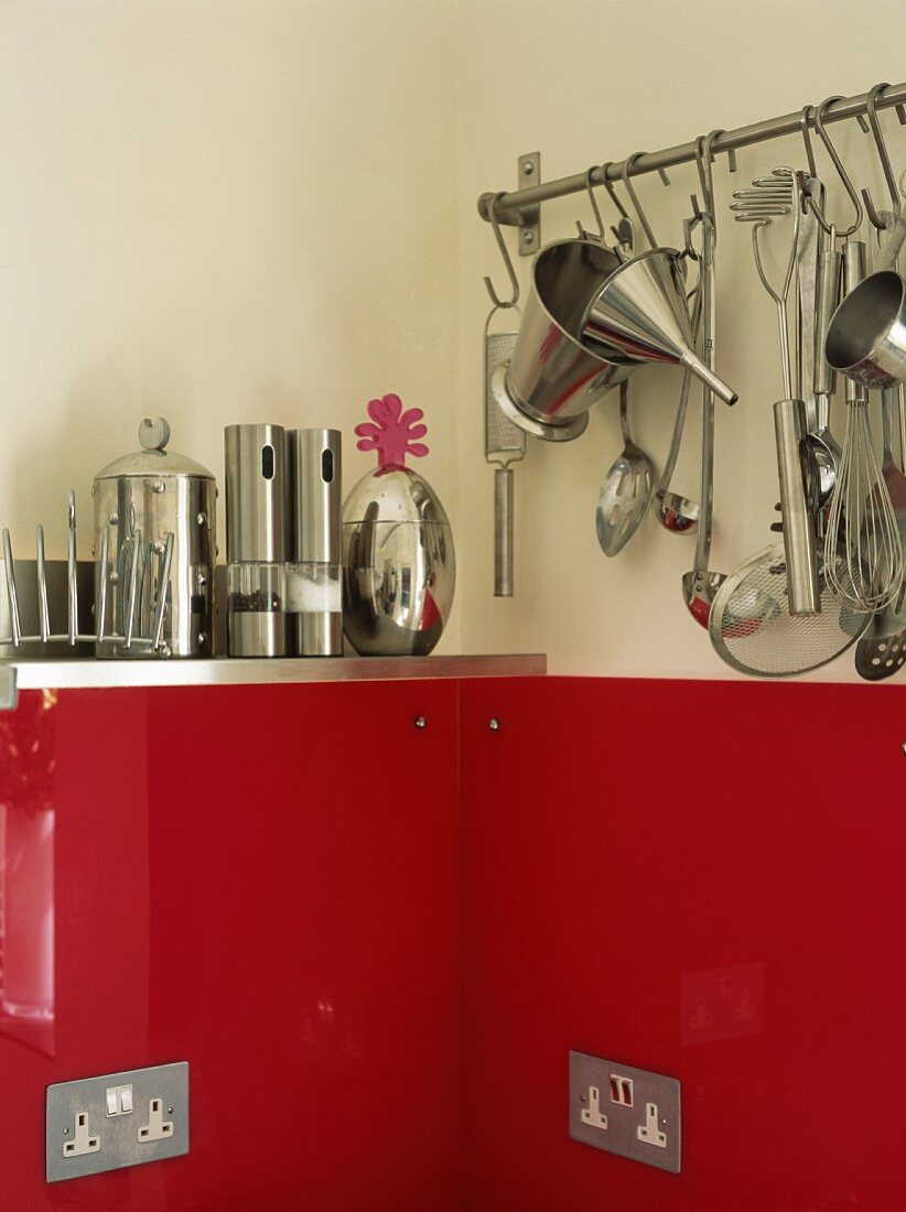 Küchengeräte an Stange und auf Bord in Edelstahl über kräftig roter Glasplatte mit integrierten Steckdosen