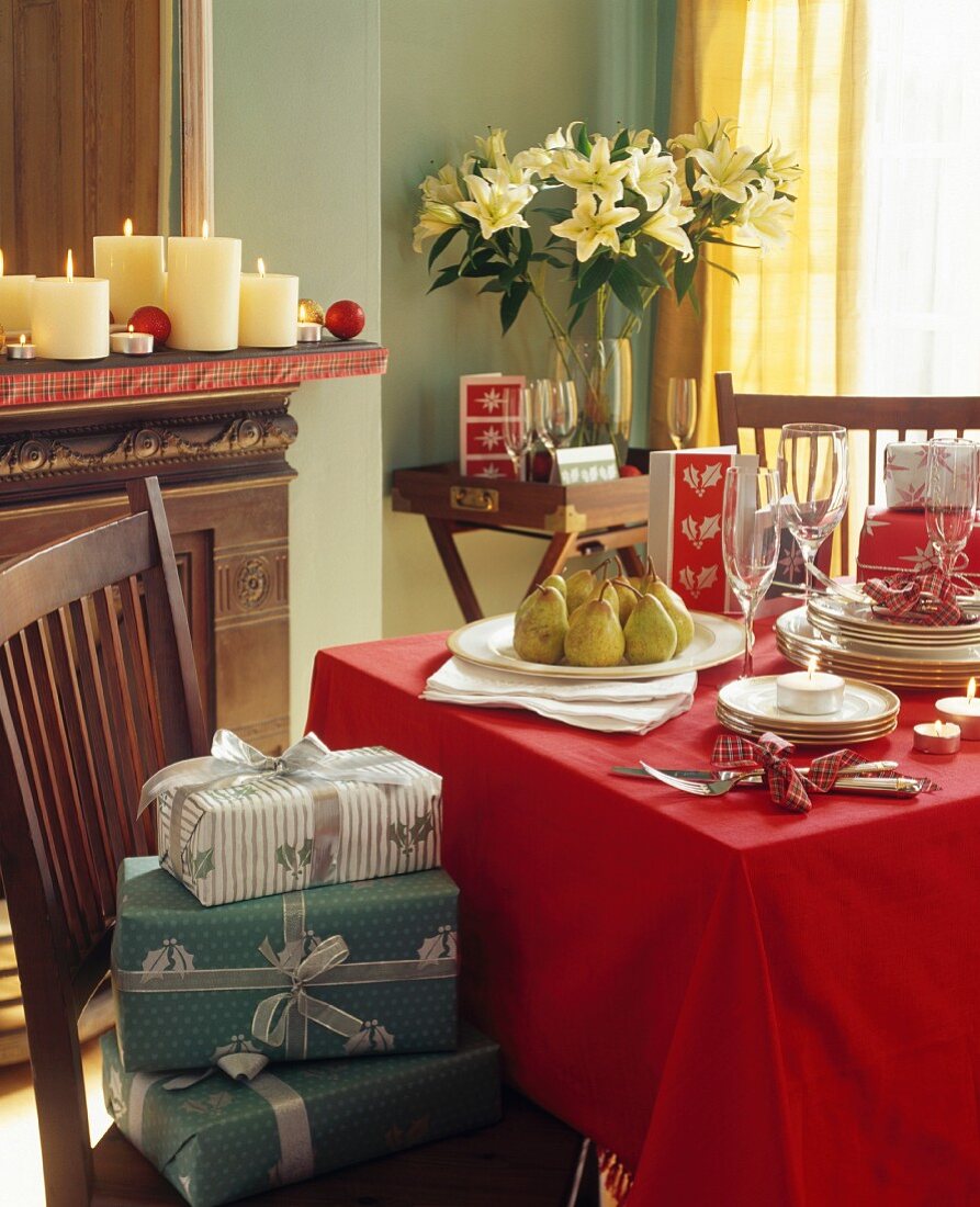 Weihnachtspäckchen auf Stuhl neben Esstisch mit Geschirrstapeln auf roter Decke