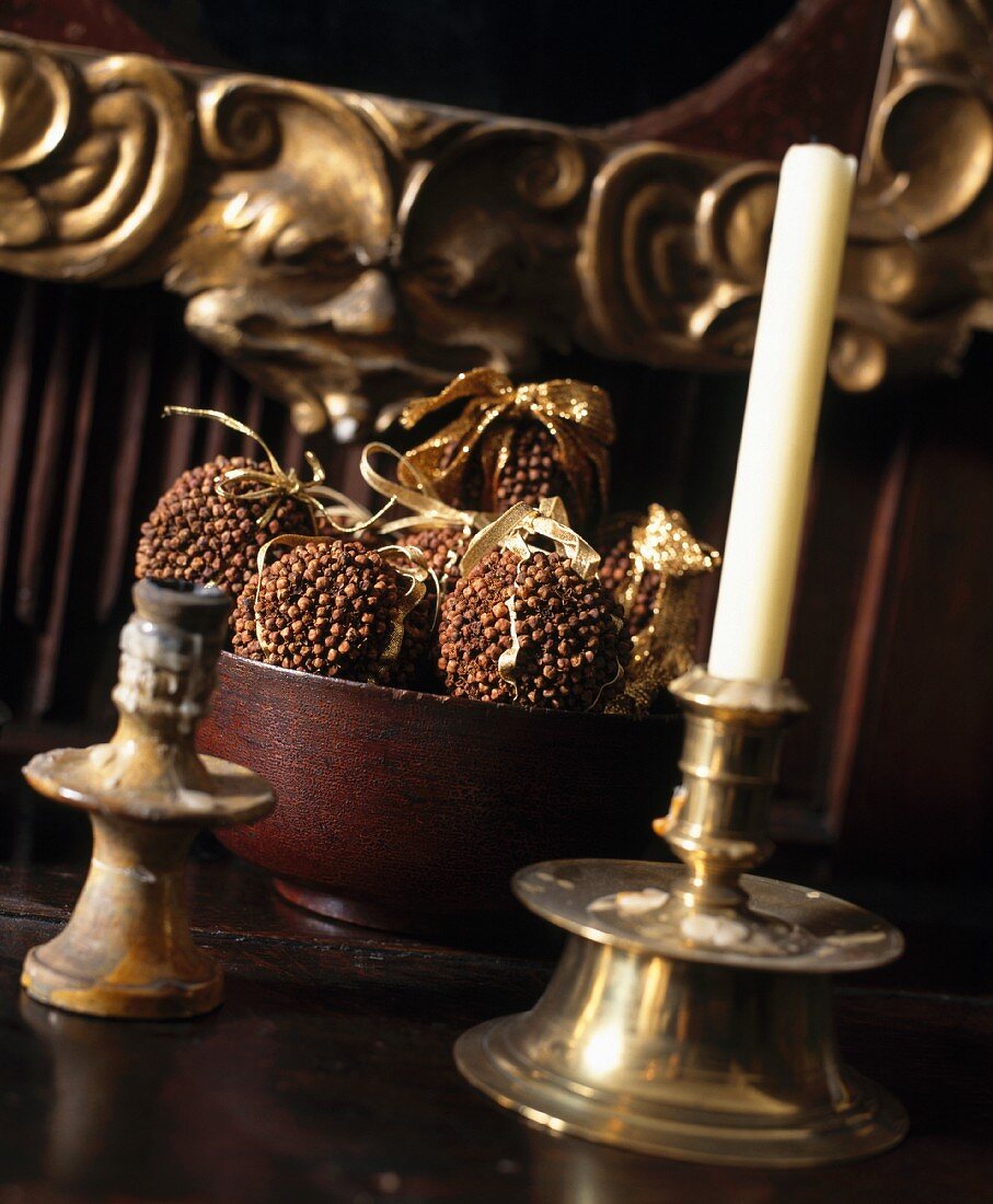 Leuchter aus Messing und Duftkugeln mit Nelken vor antiker Fratze als Detail eines vergoldeten Spiegels