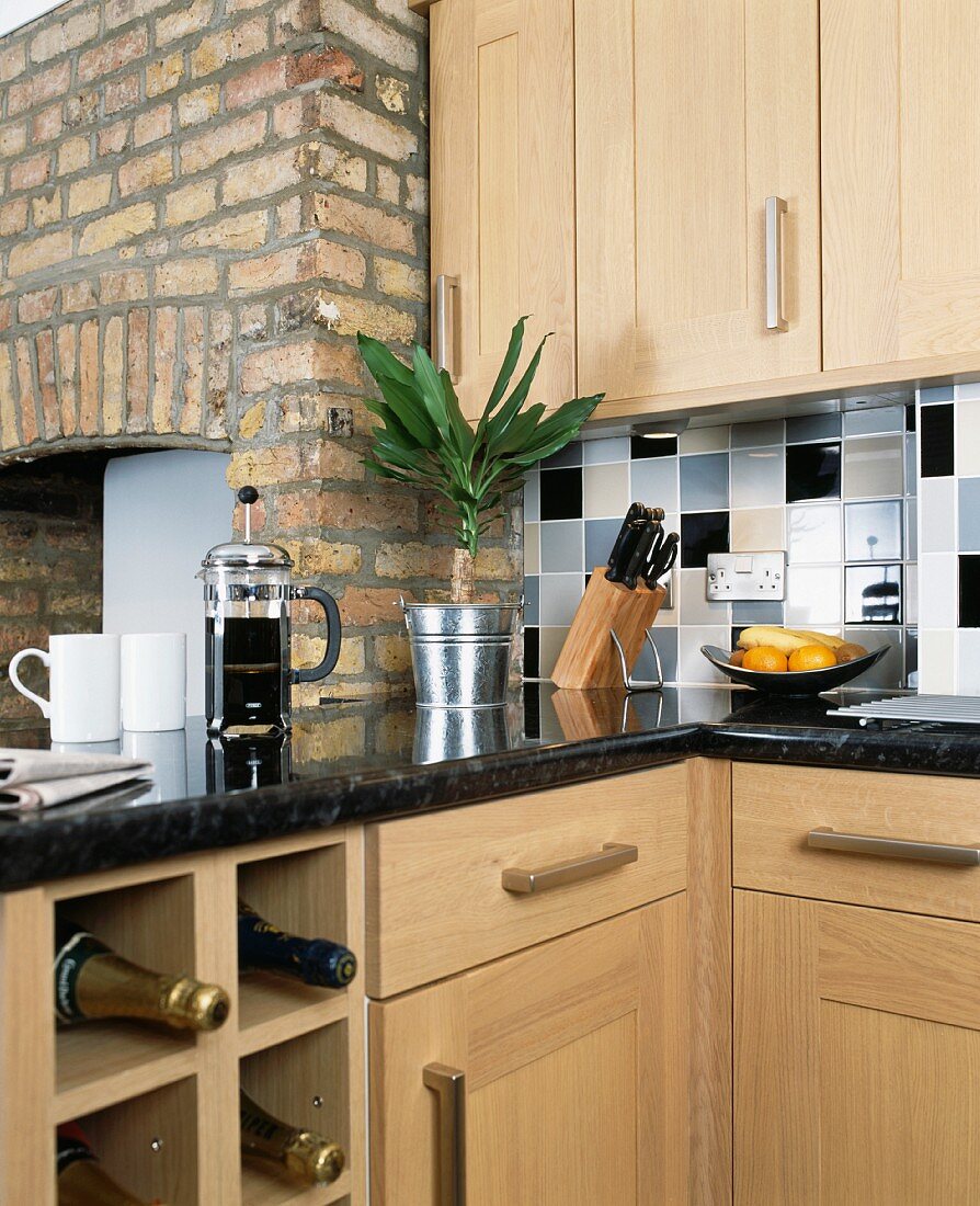 Moderne Küche aus hellem Holz und Granit-Arbeitsfläche mit Sekt in Würfelregal und Kaffeebereiter vor Kaminwand aus Backstein