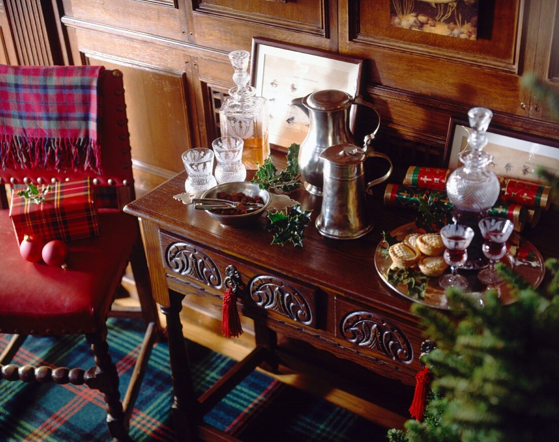 Mit Kristallkaraffen und Zinnkrügen gedeckte Stilkommode neben rot gepolstertem Stuhl mit Weihnachtspäckchen