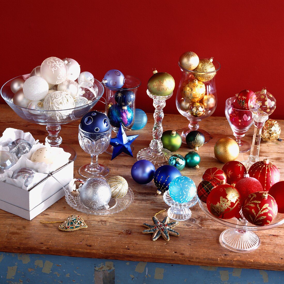 Farbig sortierte Weihnachtskugeln in Glasgefässen, Pappschachtel und lose auf Holztisch gelegt