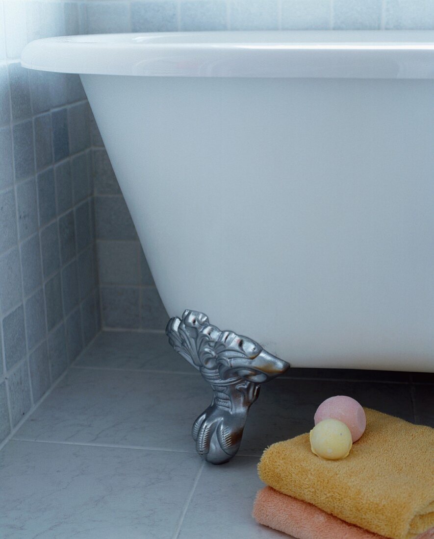 Freistehende Badewanne mit Klauenfuss neben Handtüchern auf grauem Fliesenboden